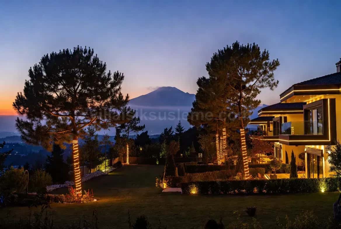 Gün batımında sırttaki villa ve ışıkla sarılmış çam ağaçları